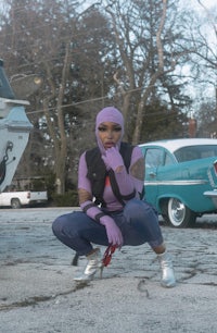 a woman in a purple outfit crouching next to a car