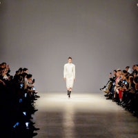 a woman walks down a runway in a white dress